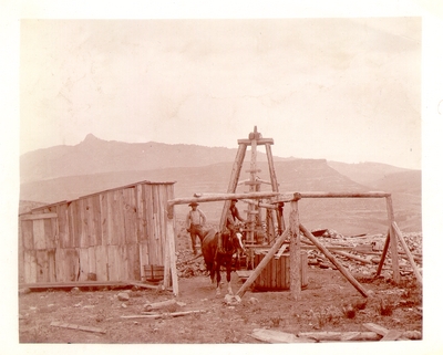 Two men and horse operating wooden drill