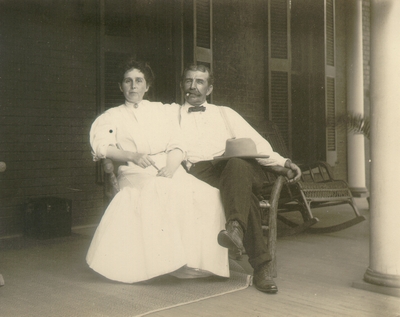 Middle-aged couple seated in wooden love seat chair on porch