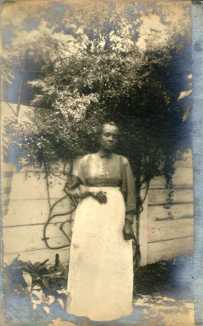 African-American woman with short hair standing in front of white fence in a garden