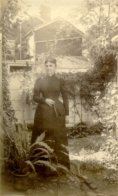 Woman in full black dress standing in garden holding a fan; variant of #196