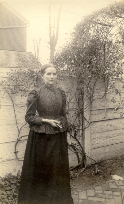 Mrs. M.C. Lyle standing in garden next to fence