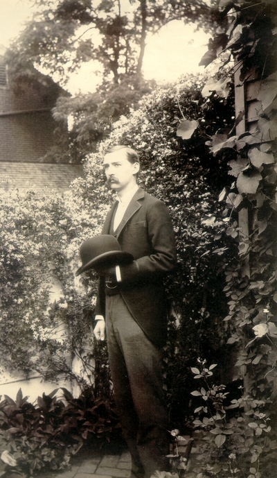 Charles Nourse Lyle standing in garden holding his hat