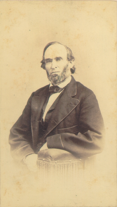 Man with graying beard wearing dark suit; Arm on cushioned rest