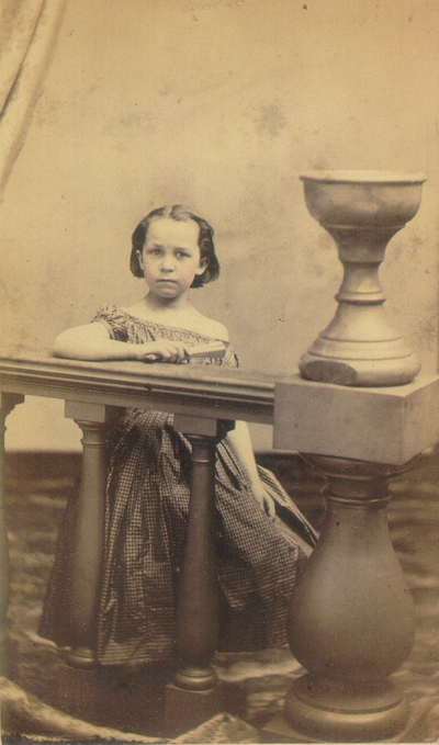 Young girl standing behind banister wearing a dress