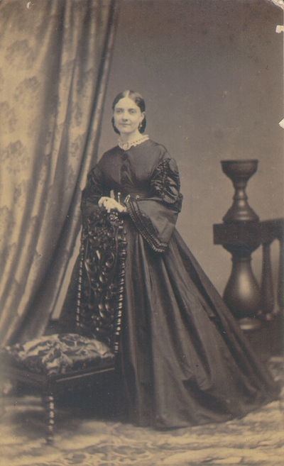 Woman wearing full black dress standing behind elaborate chair