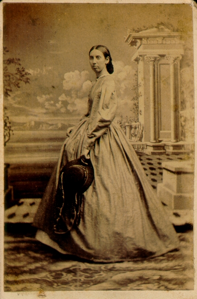 Woman wearing long dress holding a dark hat to side