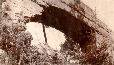 Several people sitting under natural bridge of rock