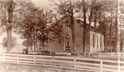 Church building with tall doors and windows surrounded by trees and white fencing; Two woman posing nearby