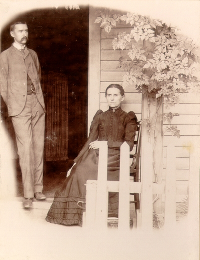 Mrs. M.C. Lyle seated on porch with her son Charles N. Lyle standing in doorway next to her