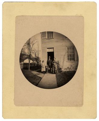 Unidentified man, woman, and child standing in front of house; removed from pg. 11 of album