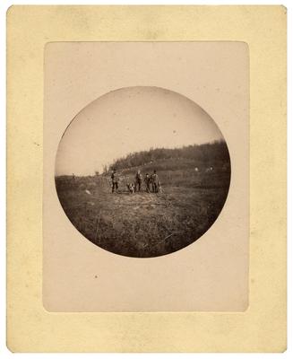 Three unidentified men with guns, three dogs and a boy standing in field; removed from pg. 20 of album