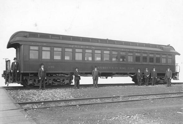 Men standing near Queen and Crescent, Agriculture Car