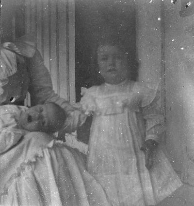 Young girl standing and infant in woman's lap