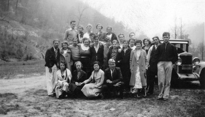 Large group of people standing in front of a car in rural area