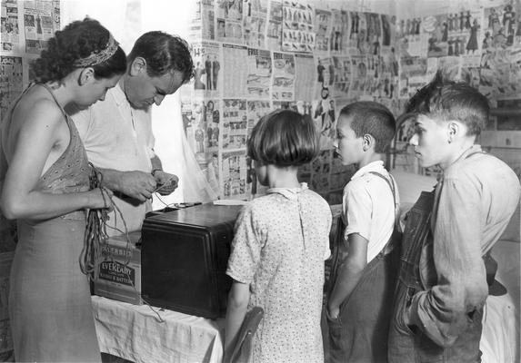 Man, woman, a young woman, and two young men observing a radio