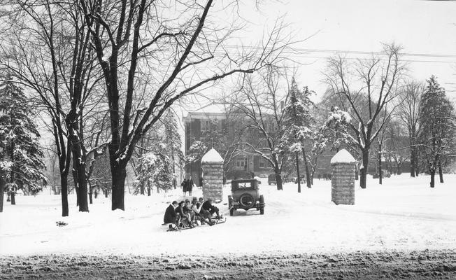 Entrance to the University of Kentucky with a car pulling students on a sled toward Frazee Hall, 1920