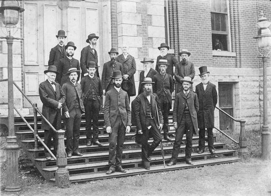 Faculty, Agricultural and Mechanical College of Kentucky, 1885, first row, left to right: W. D. Lambuth, Latin and Greek Languages, President James K. Patterson, James G. White, Mathematics, second row, left to right, John Shackleford, English, third row, left to right, Dr. Robert Peter, Chemistry, and son, Alfred M. Peter, Chemistry, fourth row, left to right, J. C. McClelland, Academy and Lieutenant L. E. Phelps, Commandant, fifth row, left to right, A. T. Parker, Microscopist, F. M. Helveti,French and German Languages, (with long white beard and glasses), Walter K. Patterson, Academy, sixth row, left to right, J. R. Potter, Pedgogy Education, (with heavy facial hair except for chin), A. T. Parker, Microscopist, seventh row, left to right, A. E. Menke, Agriculture Chemistry, A. R. Crandall, Natural History, Maurice Kirby, Philosophy, John H. Neville, Greek and Latin, with no hat and in the window, James K. Patterson's son, William A. Patterson, print dated 1885