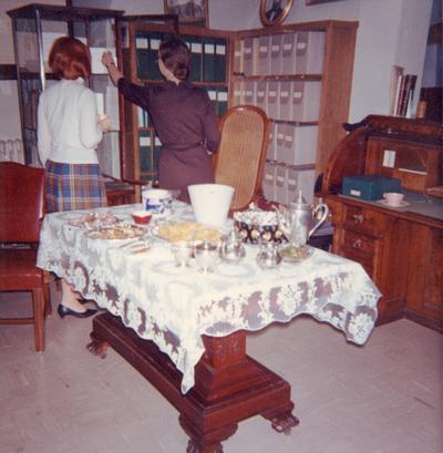 University Archives staff: unidentified woman and University Archivist, Mary Hester Cooper with exhibit cases, President Patterson's desk and chair, and a table from his office set for a departmental party, circa 1956 - color print, Photographer, Unknown
