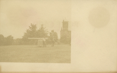 postcard, 2 unidentified men standing next to cannon on UK campus, building off in the distance