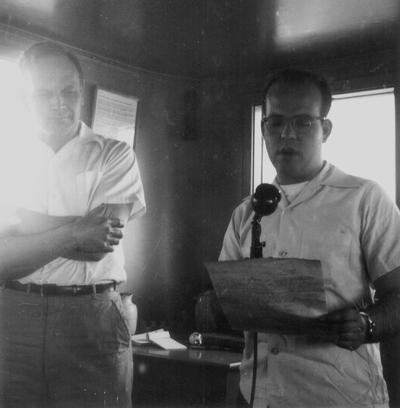 Two men standing, reading into microphone
