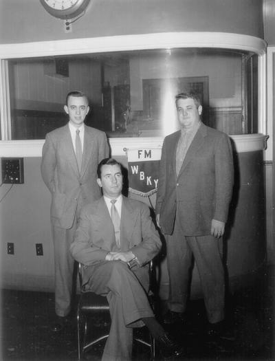 Three men posed in front of WBKY banner with engines studio in background. (Jack McGeehan, seated)