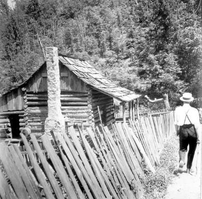 Man walking down dirt road next to log cabin