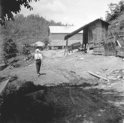 Man walking down dirt road, next to wagon and shed