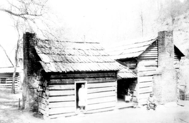 Woman with elderly woman and man, outside of log cabin with additional room added