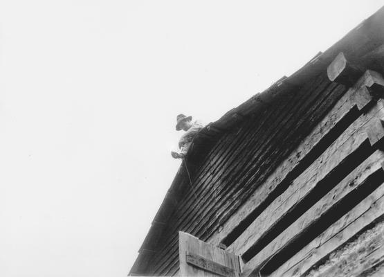 Man on roof of a log building, working on wiring