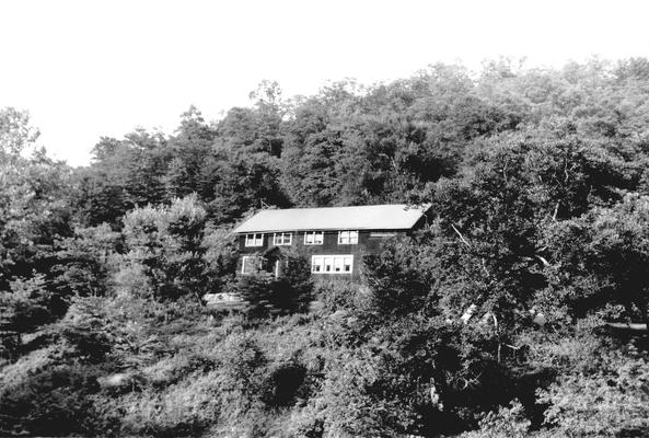 Large, two-story house on a slope, with trees