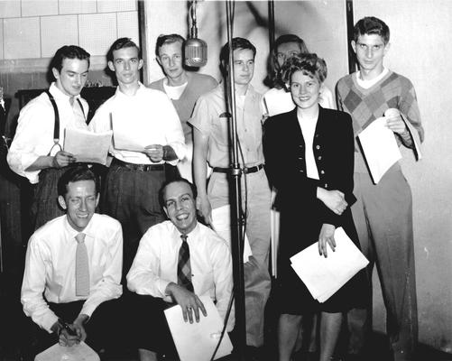 Group of students standing around microphone with scripts in hand