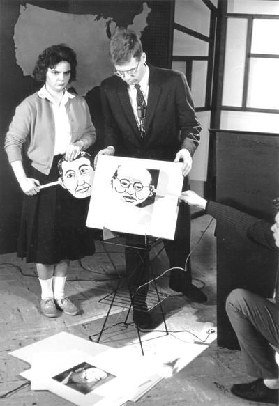 Shirley Boyd and Dr. Doug Schwartz  going through still photos on cards; woman holding cartoon-like face on stick; man squatting, holding different cartoon-like face in front of photo