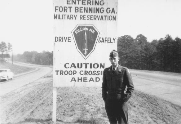 Young man in uniform at sign, designating entrance to Fort Hoenig; Fort Hoenig, GA