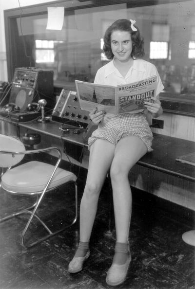 Young woman sitting on counter of control booth reading 