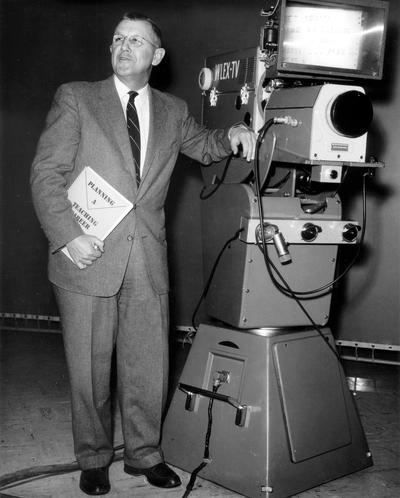 Dr. Ellis Hartford leaning on WLEX-TV, Channel 18 studio camera; Lexington, KY