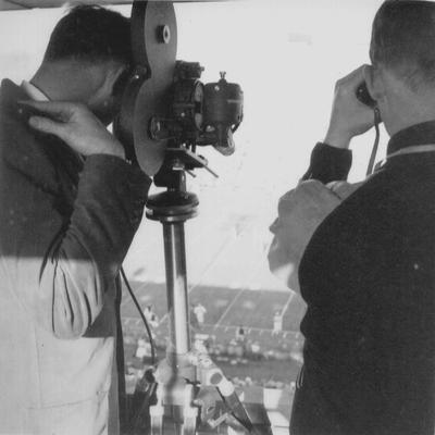 Ric Sanderson filming a football game at Stoll Field; man standing next to him looking through binoculars