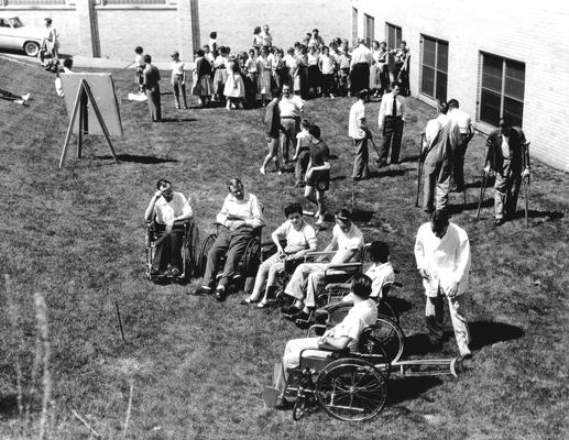 Patients on the grounds of a rehabilitation hospital; group of young children in background are possibly on a field trip