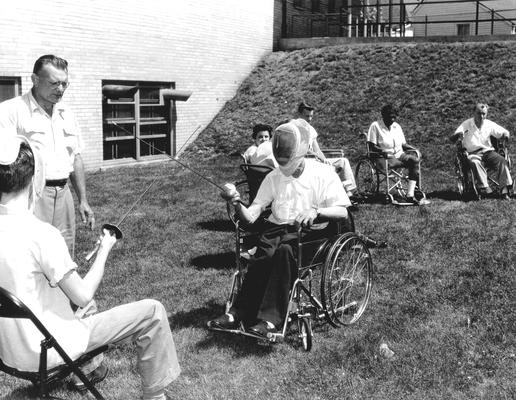Two people fencing, one in a wheelchair; patients outside of rehabilitation hospital