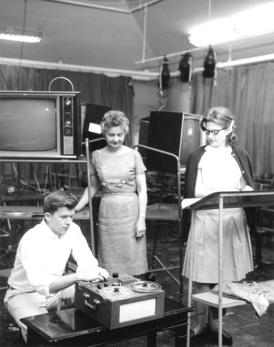 Two women (Elizabeth Taylor?) watching young man work reel to reel tape machine