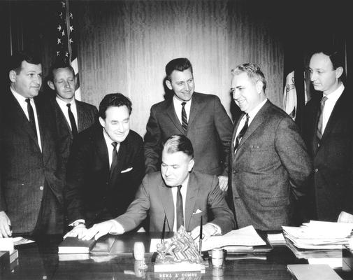Kentucky Governor Bert T. Combs at desk, future Governor Louie B. Nunn leaning over, Len Press at far right, 4 unidentified men; Frankfort, KY (L to R: Bill Small, WHAS News Director; Ron Stewart, WBKY Chief Engineer; Harry King Lowman, Speaker of the House; Townes Ray, Majority Leader of the House; Wendell Butler, press)