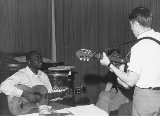 African-American man sitting on piano bench playing guitar with young man
