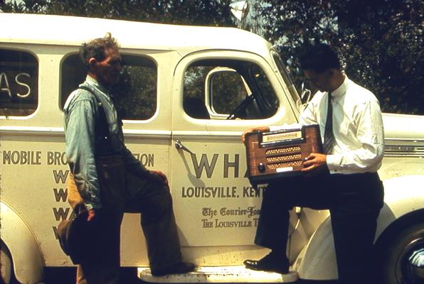 Two men standing next to WHAS truck looking at radio