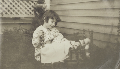 A very young girl sitting outdoors; on the back: 