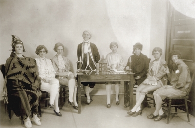 Group photo of eight women dressed in costumes, sitting around a table