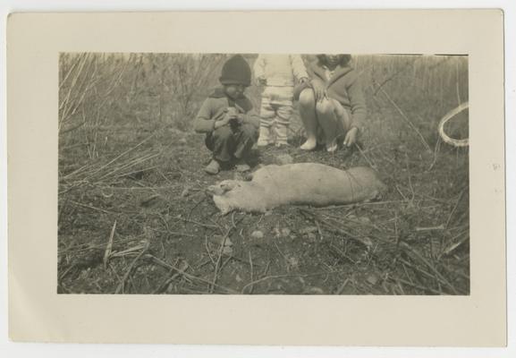 Three unidentified children crouching next to a dead dog