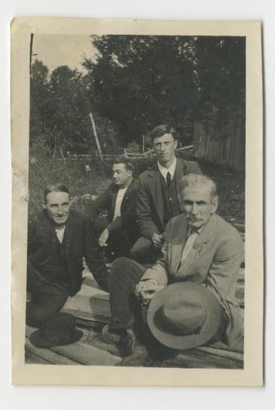 Four unidentified men sitting on a lumber pile