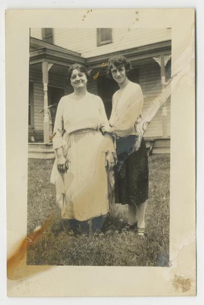 Two unidentified women standing in the yard in front of a house