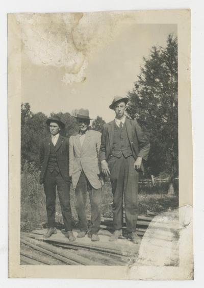 Three unidentified men standing on a pile of lumber