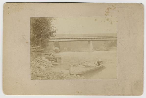 Wooden bridge and bank of KY River with boat in Frankfort, KY; The wooden bridge at Frankfort, taken by Paul, Aug. 1886 written in ink on back