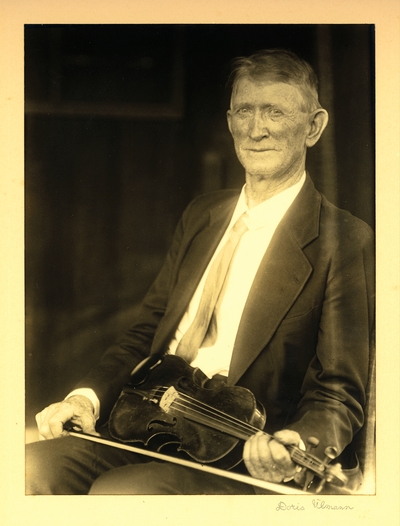Mr. Bryant; Brasstown, North Carolina.  Man in coat and tie, seated with fiddle